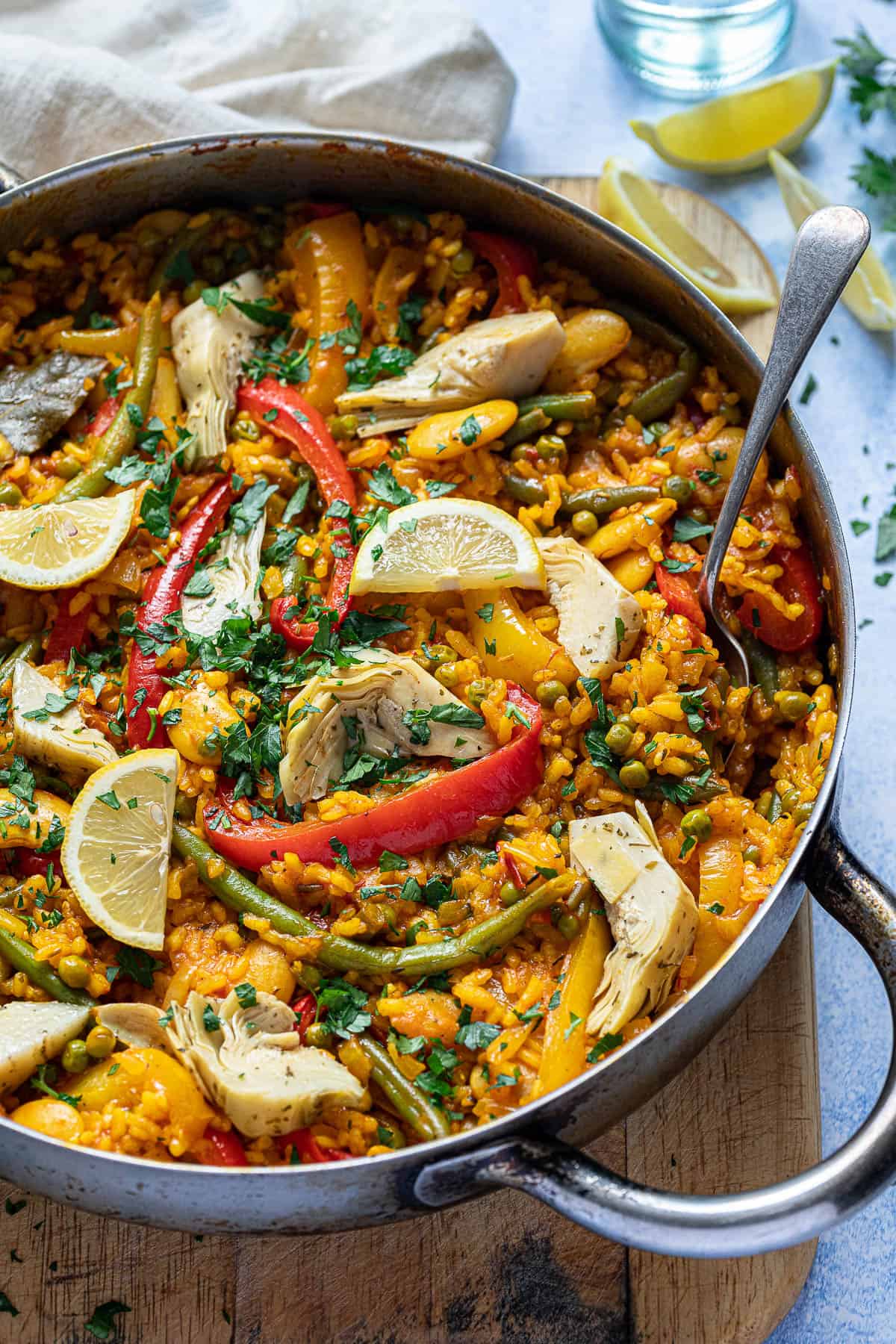 Close up of a pan of vegetable paella on a wooden board.