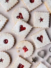 Vegan Linzer cookies on a marble background, one with a bite taken out of it.