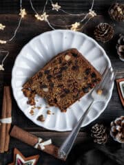 A slice of gluten-free vegan Christmas cake on a white plate with a forkful removed.