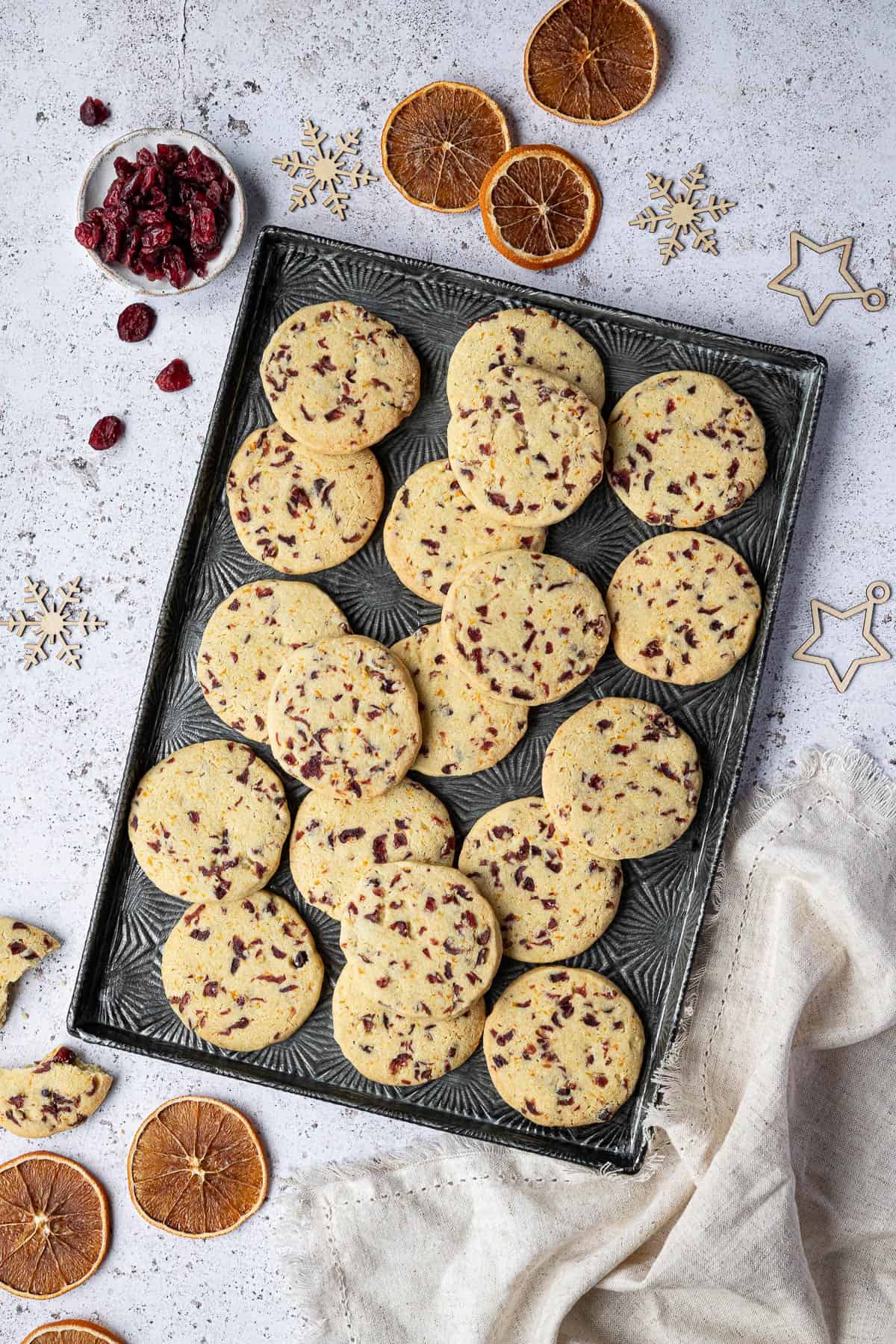 Shortbread cookies on a metal tray with dried orange slices, cranberries and Christmas ornaments.