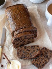 Sliced vegan malt loaf on a sheet of baking parchment with cups of tea and a bowl of butter.