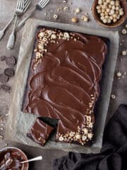 Chocolate hazelnut sheet cake on a brown surface with bowls of hazelnuts and ganache.