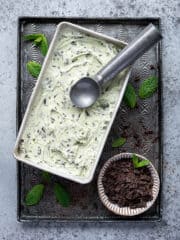 Vegan mint choc chip ice cream in a metal loaf tin on a baking tray with a bowl of chocolate.