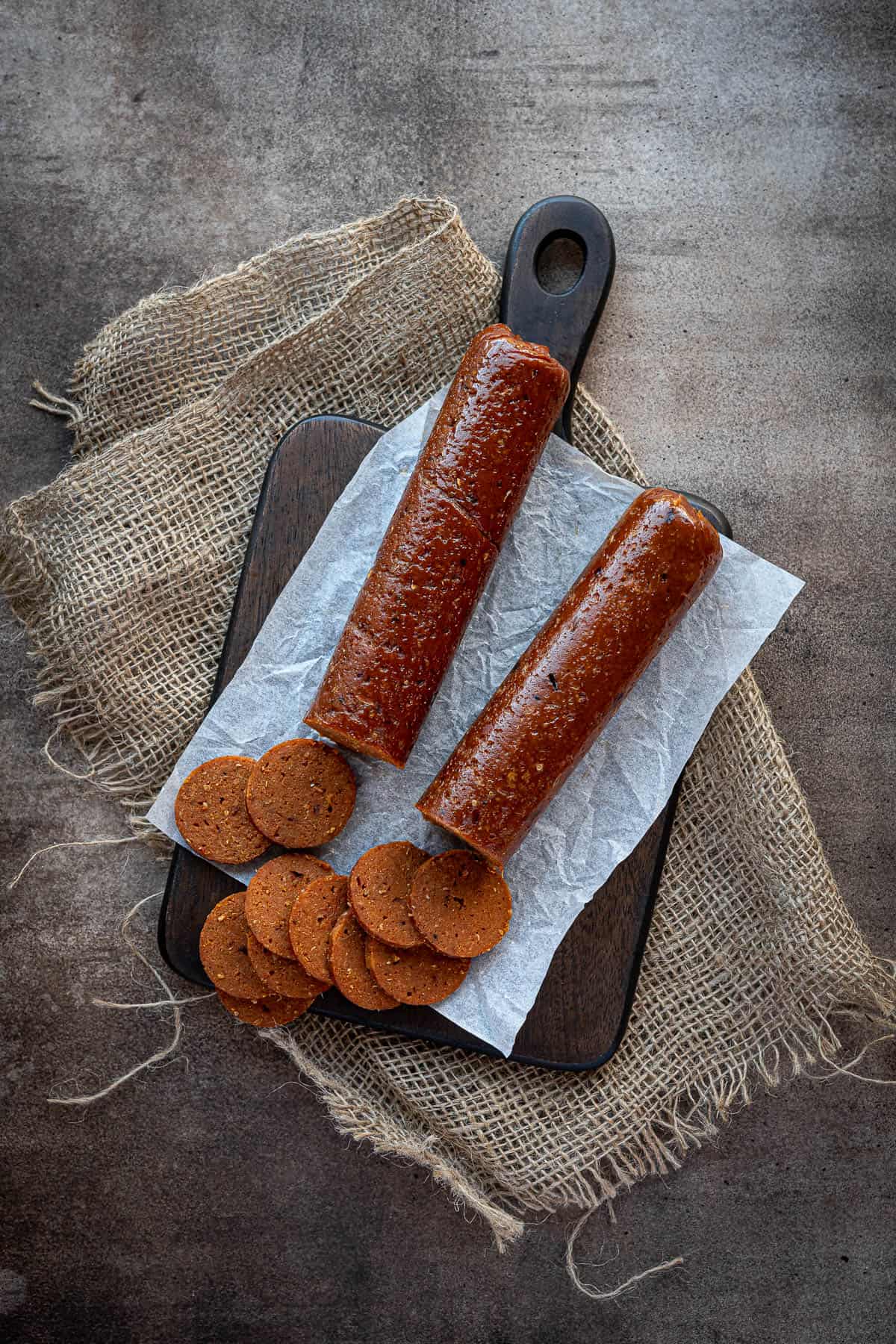 Two seitan pepperoni sausages on a wooden serving board.