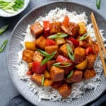 Sweet and sour tofu on top of rice in a grey bowl.