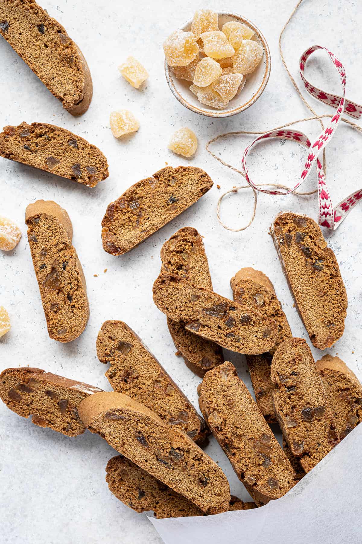 Vegan ginger biscotti in a white bag with a bowl of ginger and ribbons.