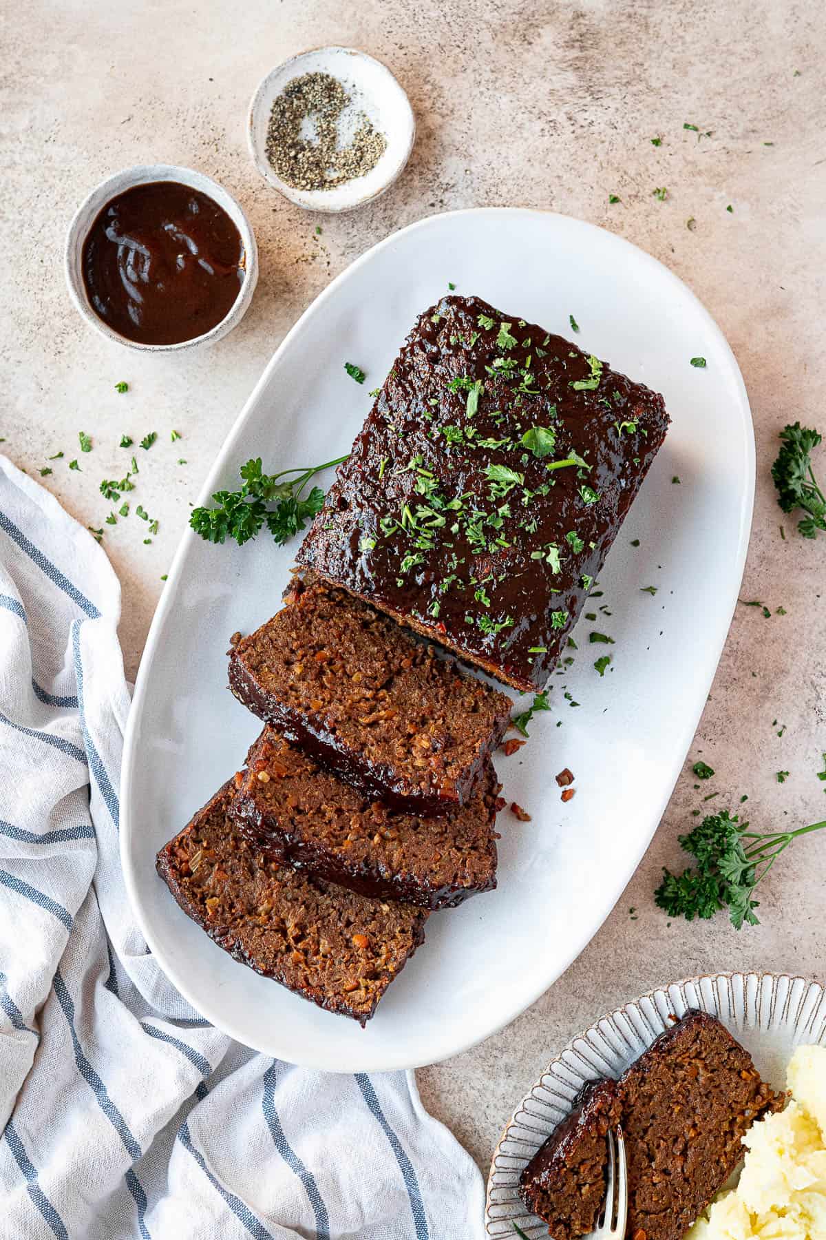 Vegan seitan meatloaf on a plate with bowls of barbecue sauce and pepper.
