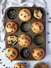 Chocolate chip muffins in a muffin tin with chocolate chips.