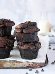 A stack of vegan double chocolate muffins on top of a baking tray with milk bottles in the background.