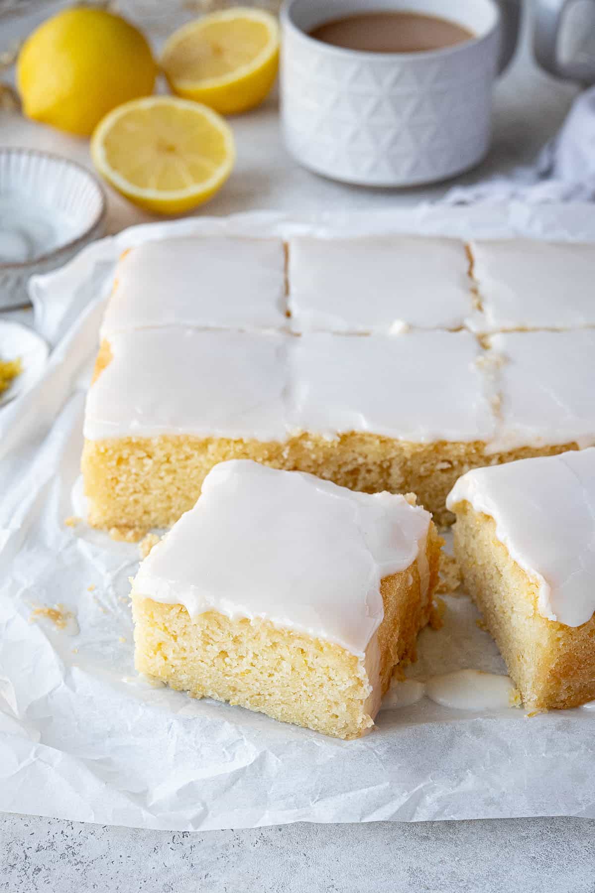 Lemon drizzle cake with cups of tea and fresh lemons in the background.