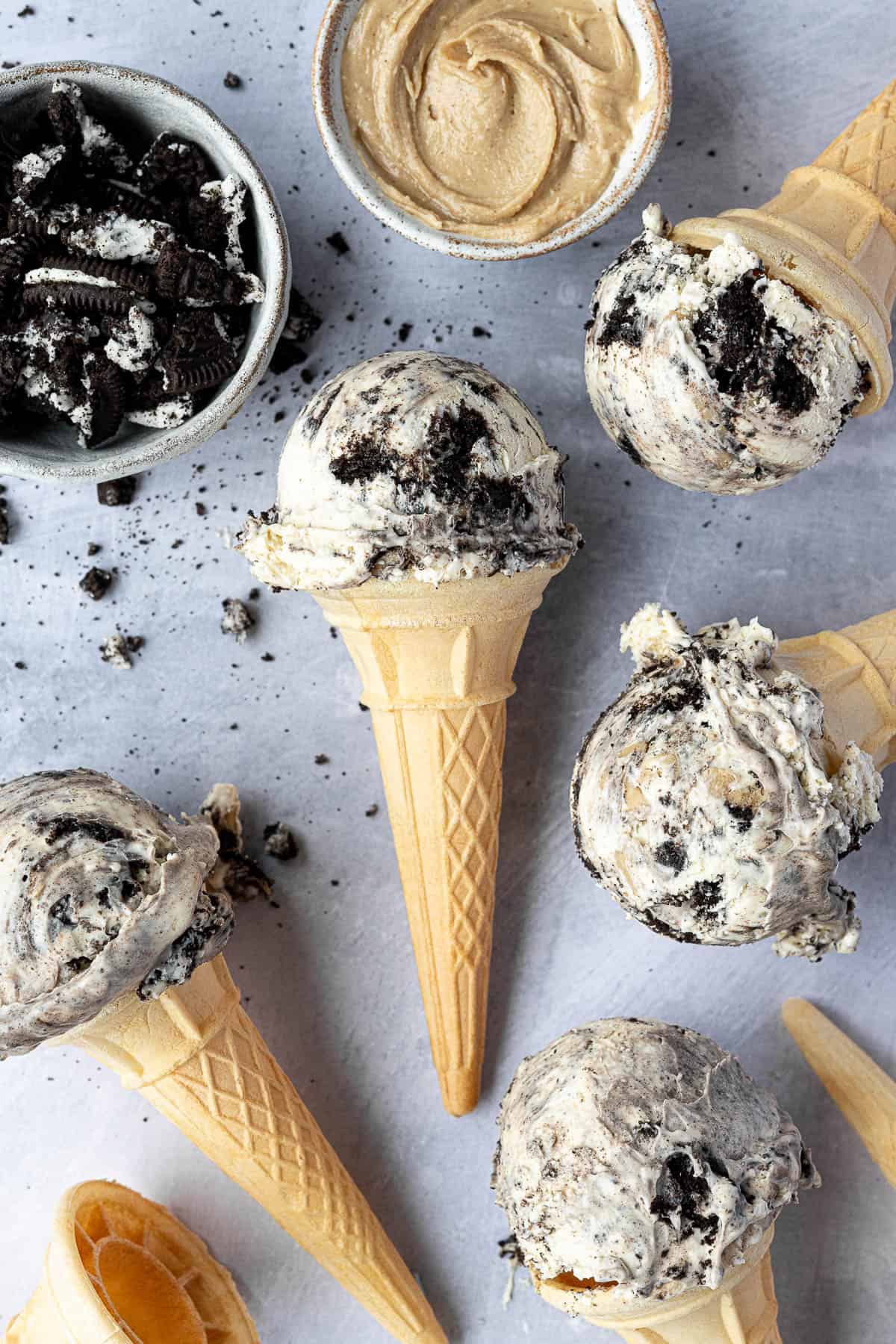 Cones of no-churn peanut butter oreo ice cream with bowls of peanut butter and crushed oreos.