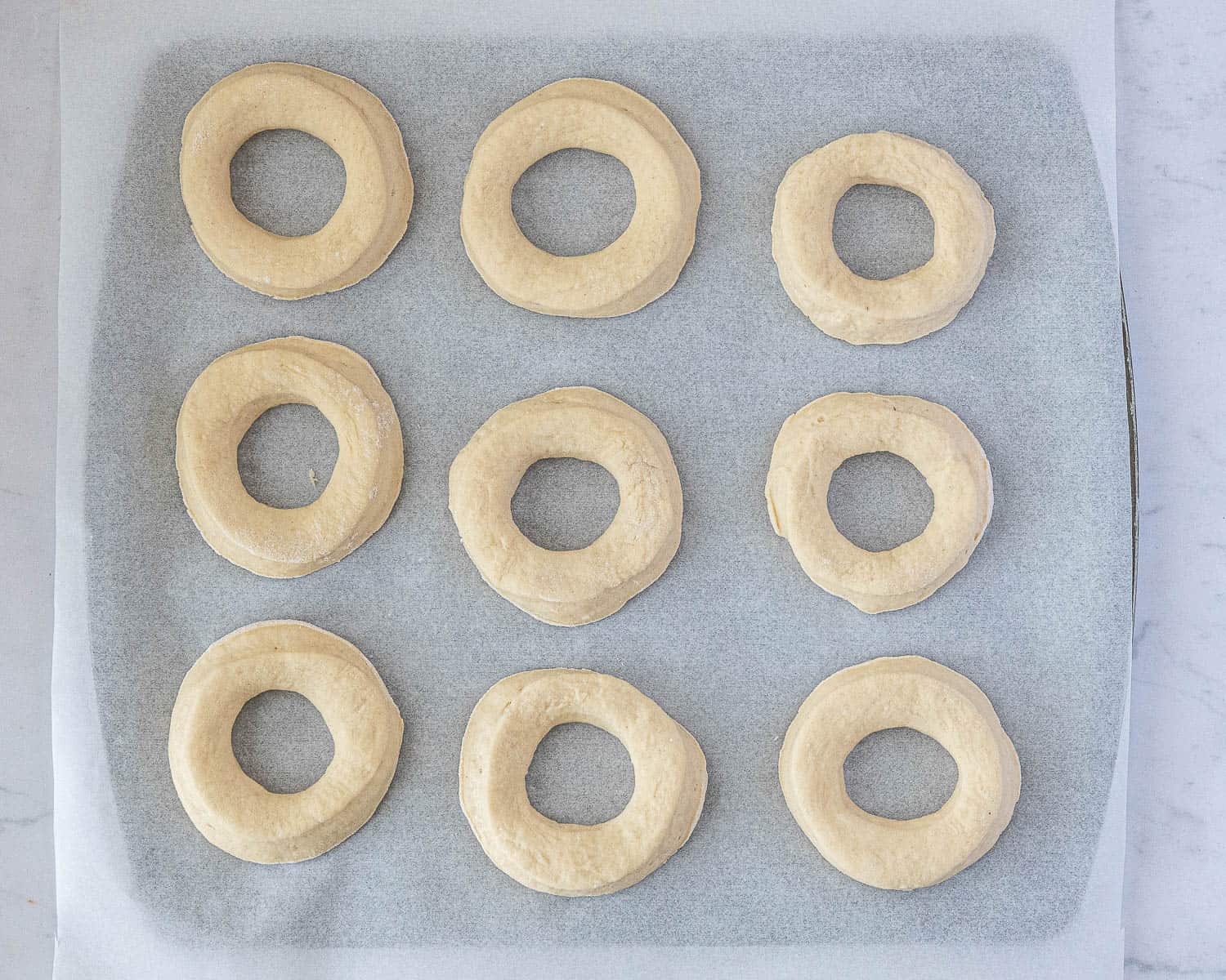 The shaped doughnuts on a baking sheet.