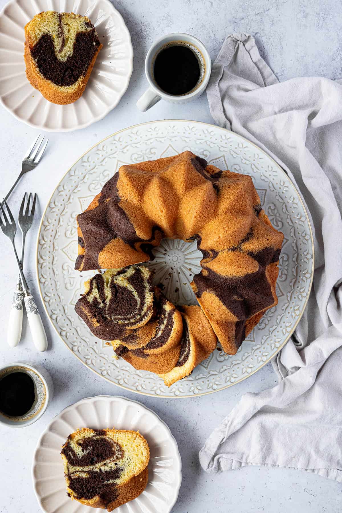 Chocolate orange bundt cake on a white plate with plates of cake and cups of coffee.