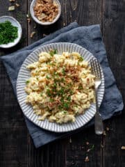 Vegan spaetzle with cheese sauce, crispy fried onions and parsley on a white plate.