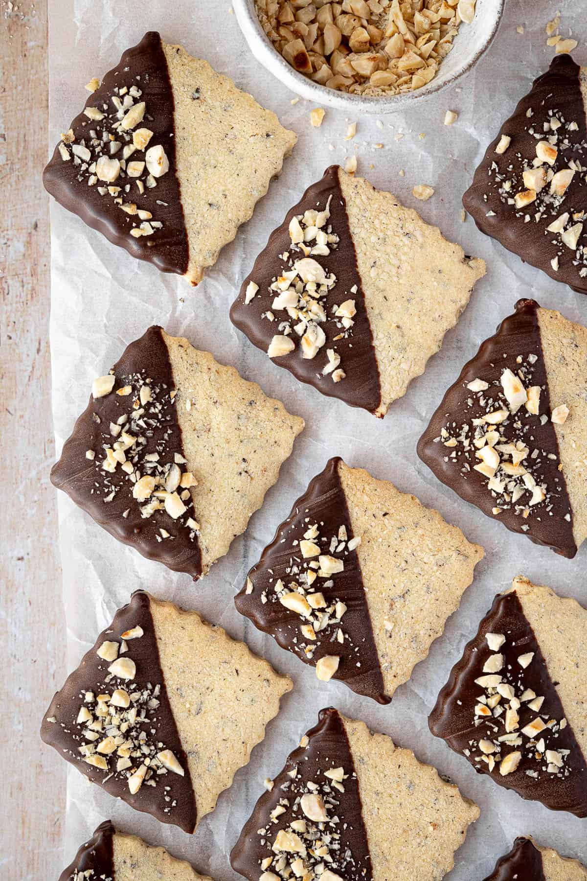 Vegan hazelnut shortbread on a sheet of baking parchment with a bowl of chopped hazelnuts.