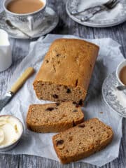 Easy marmalade tea loaf on a sheet of baking parchment with cups of tea and a bowl of butter.