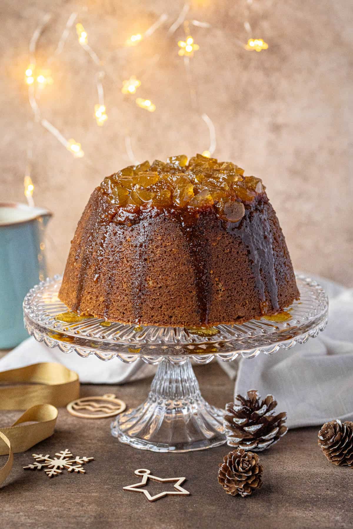 Steamed gingerbread pudding on a glass cake stand with Christmas lights and decorations.