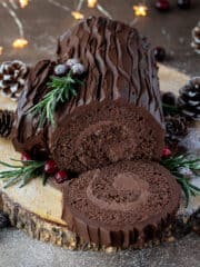 Vegan chocolate yule log with a slice cut on a wooden board with festive decorations.