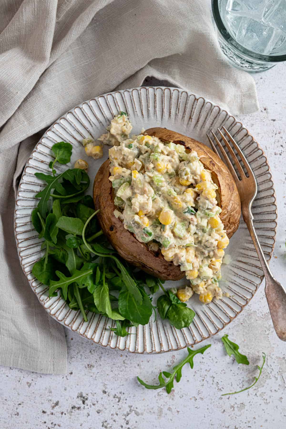 A baked potato with chickpea mayo salad and some green salad on the side.