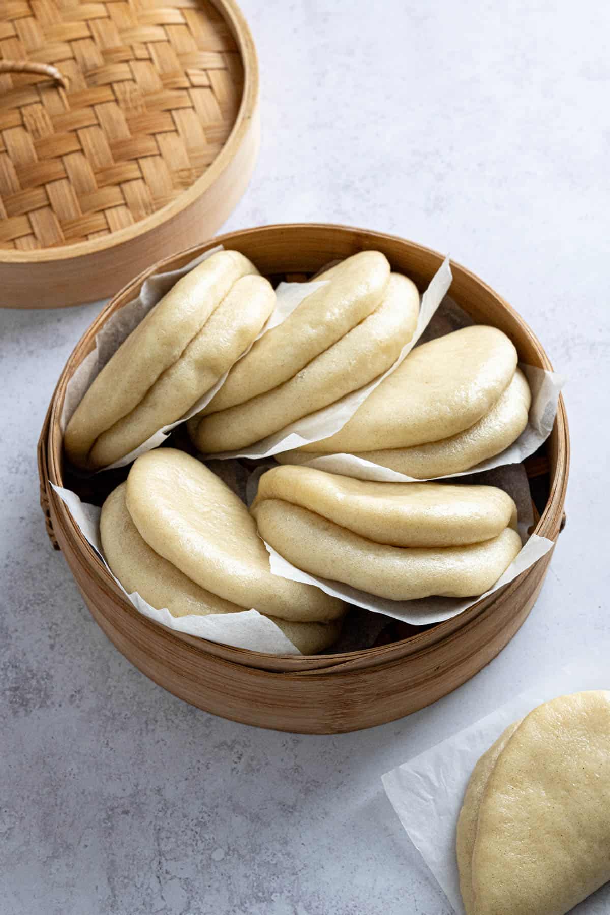 A pile of bao buns in a bamboo steamer.