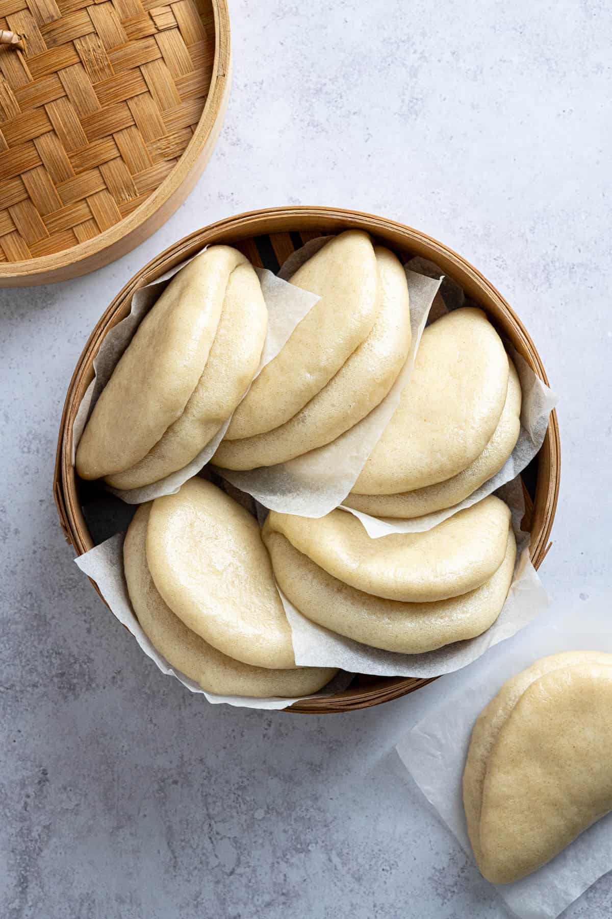 Bao buns on pieces of baking paper in a bamboo steamer.