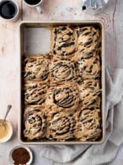 Mocha cinnamon rolls in a pan with one removed, with cups of coffee and a caffetiere.