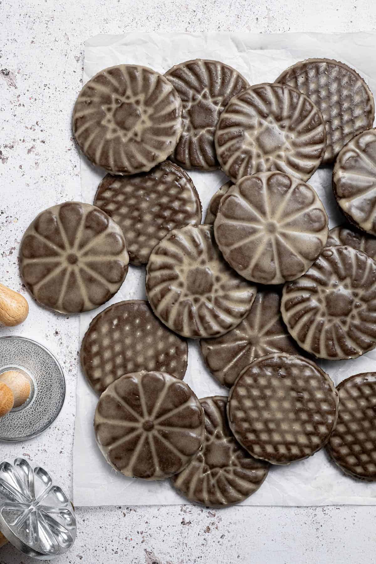A pile of vegan glazed gingerbread cookies on a sheet of baking paper with metal cookie stamps next to them.