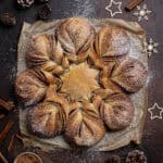 Vegan cinnamon star bread on a dark surface surrounded by cinnamon sticks, pine cones and Christmas decorations.
