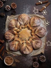 Vegan cinnamon star bread on a dark surface surrounded by cinnamon sticks, pine cones and Christmas decorations.