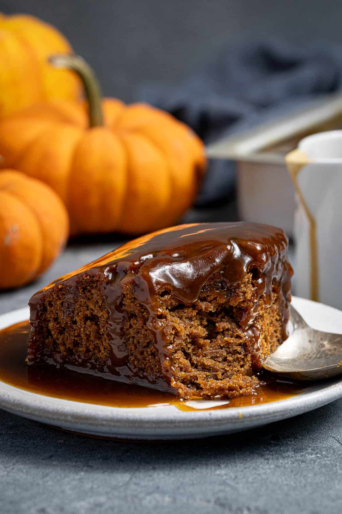 A square of vegan pumpkin sticky toffee pudding on a plate with a spoonful removed.