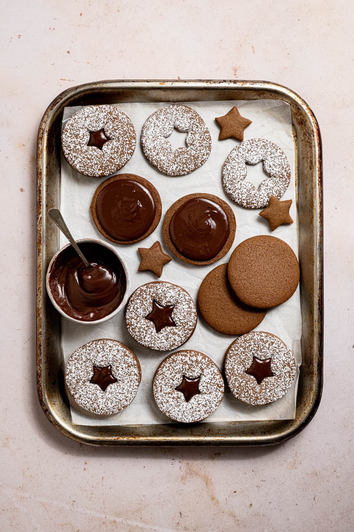 Chocolate gingerbread sandwich cookies on a metal tray with a bowl of ganache.