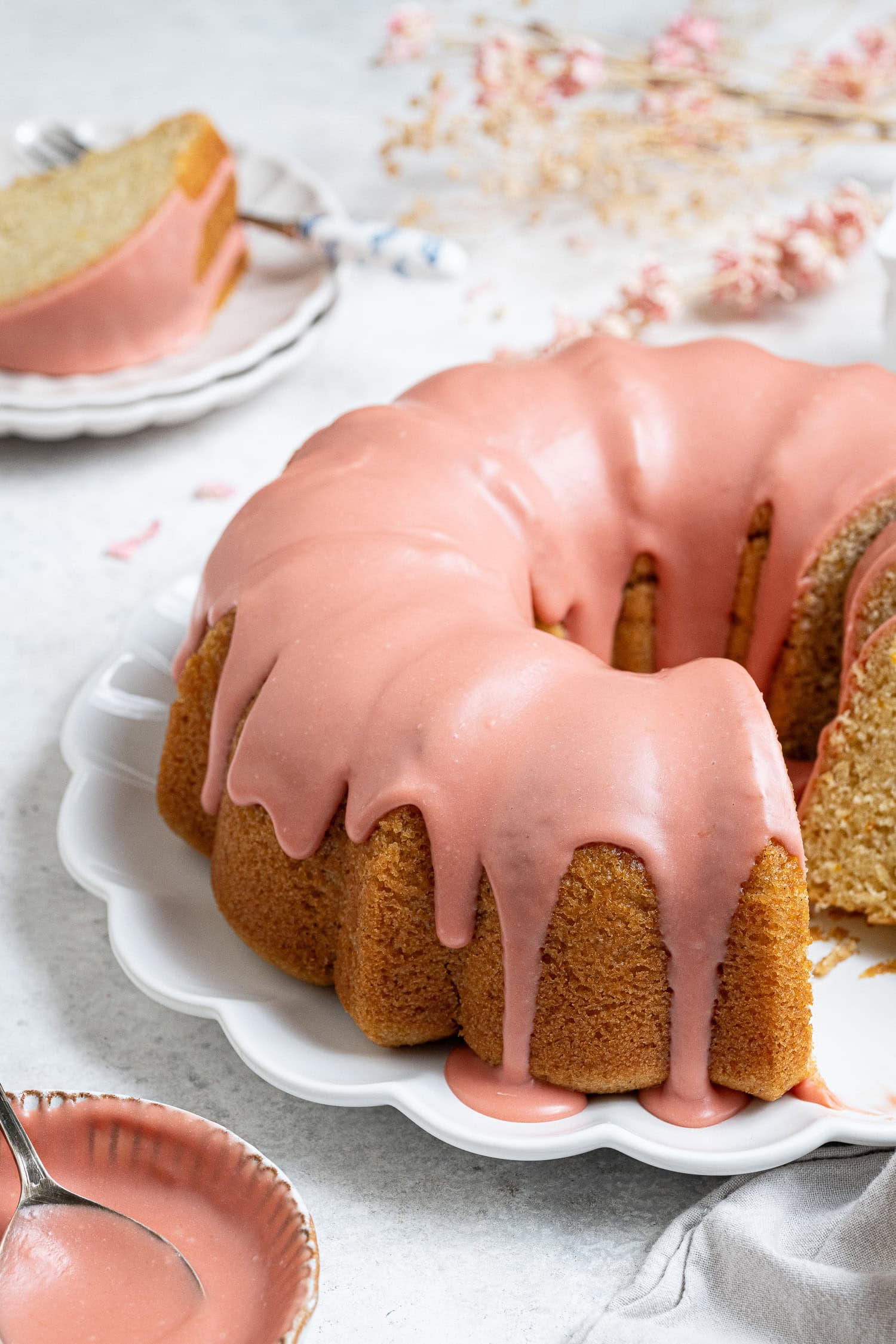 The sliced blood orange bundt cake on a white plate with a plate with a slice of cake on it in the background.