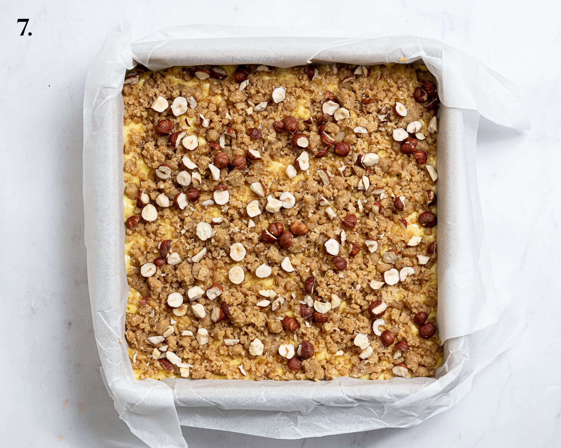 Step 7, the batter in the tin topped with the crumble and hazelnuts.