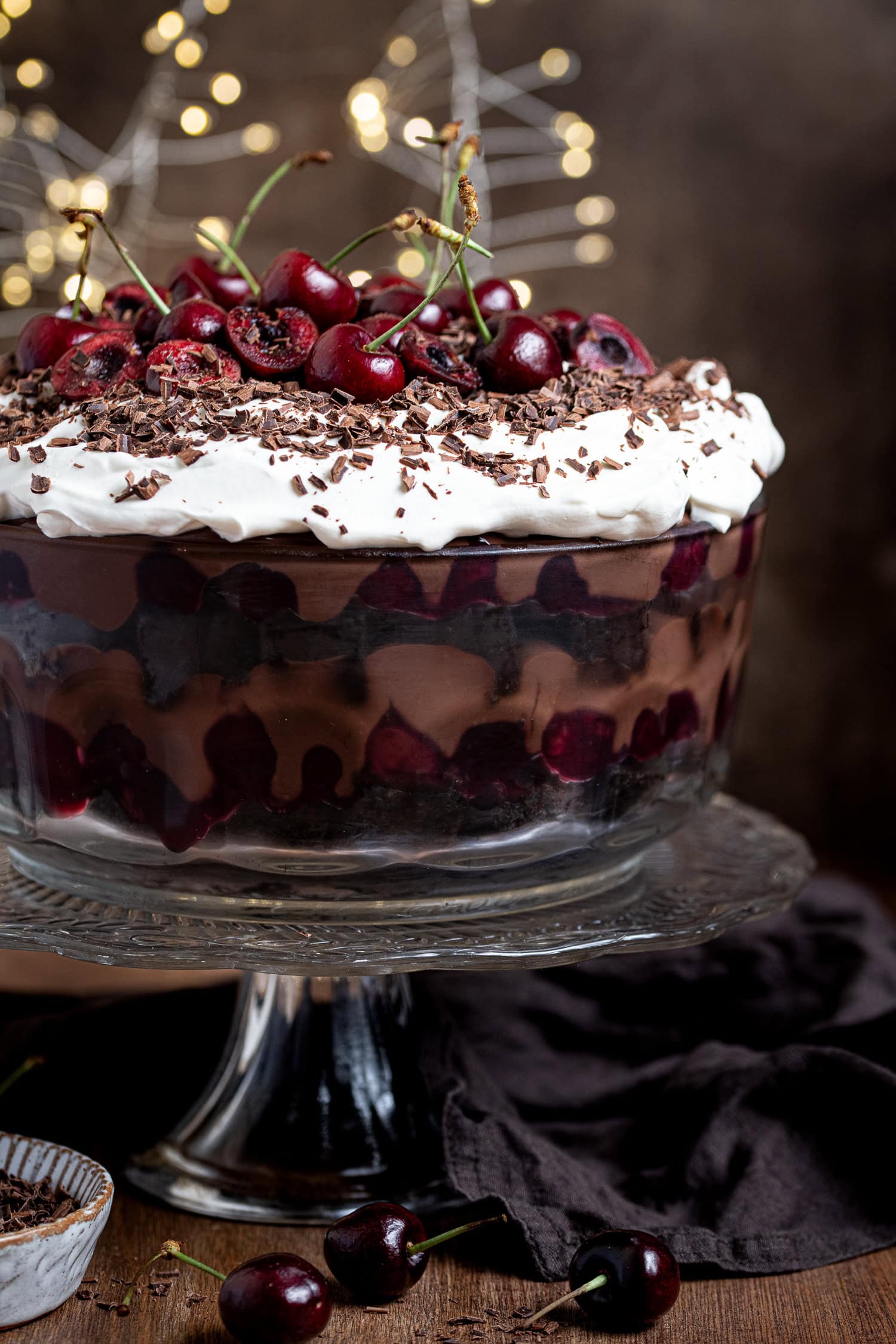 Vegan black forest trifle topped with fresh cherries and chocolate shavings, on a glass cake stand.