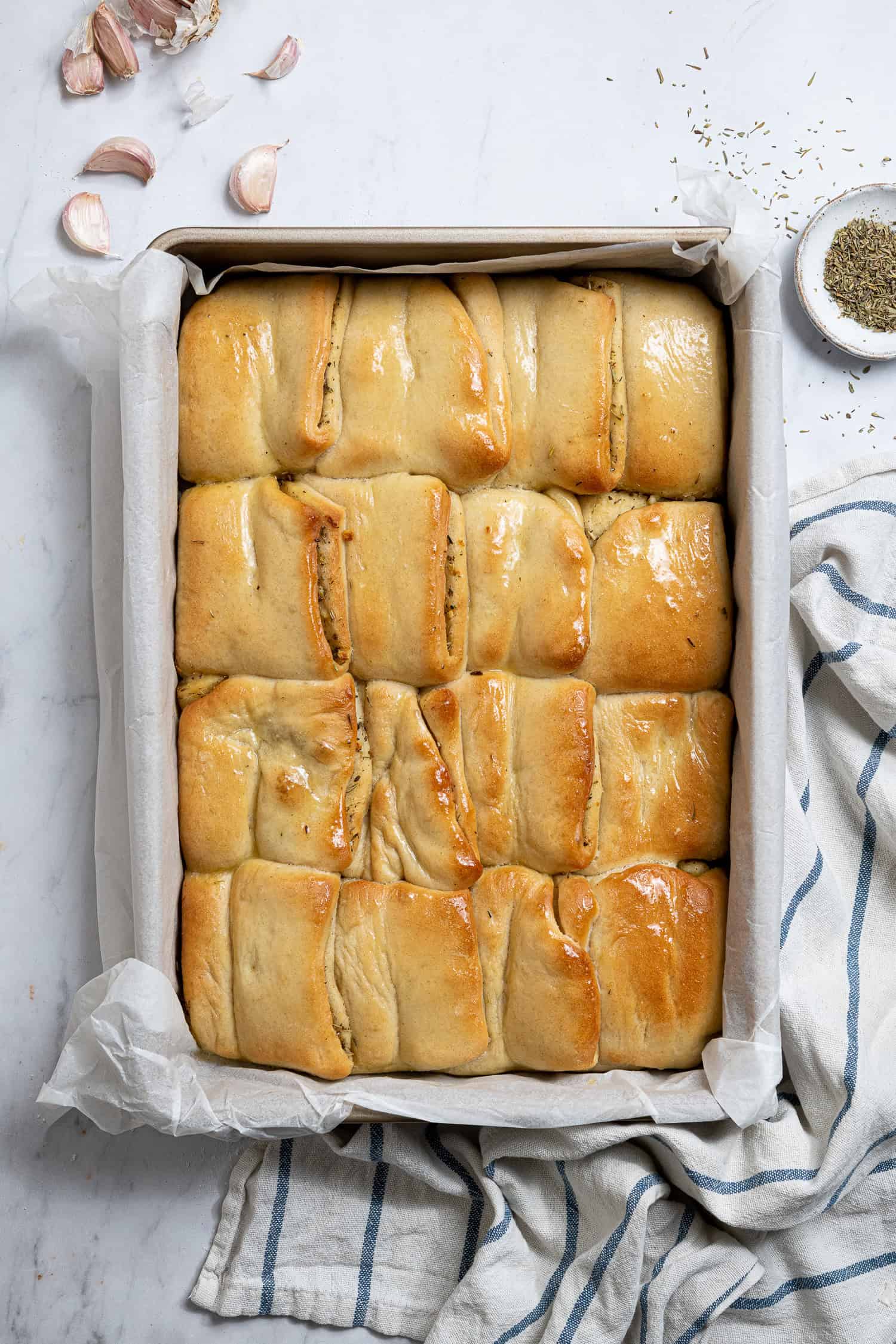 A pan of baked garlic Parker House rolls brushed with melted butter.