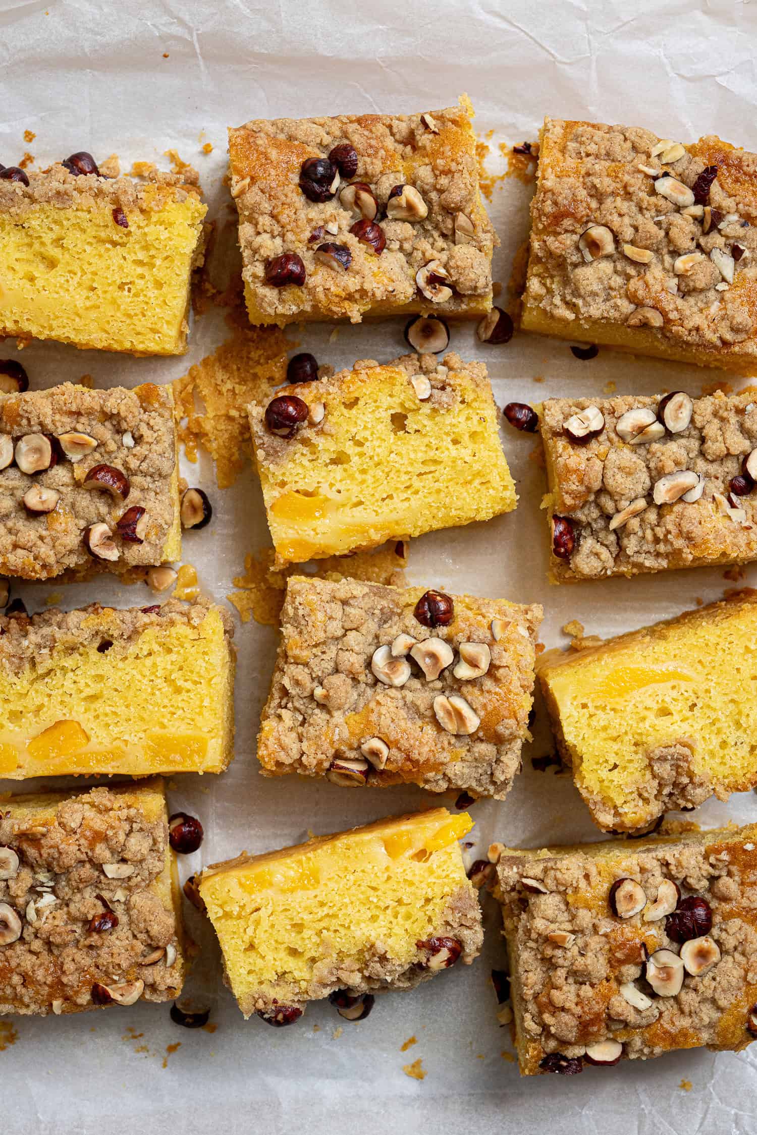 Squares of vegan peach crumble cake on a sheet of baking paper.