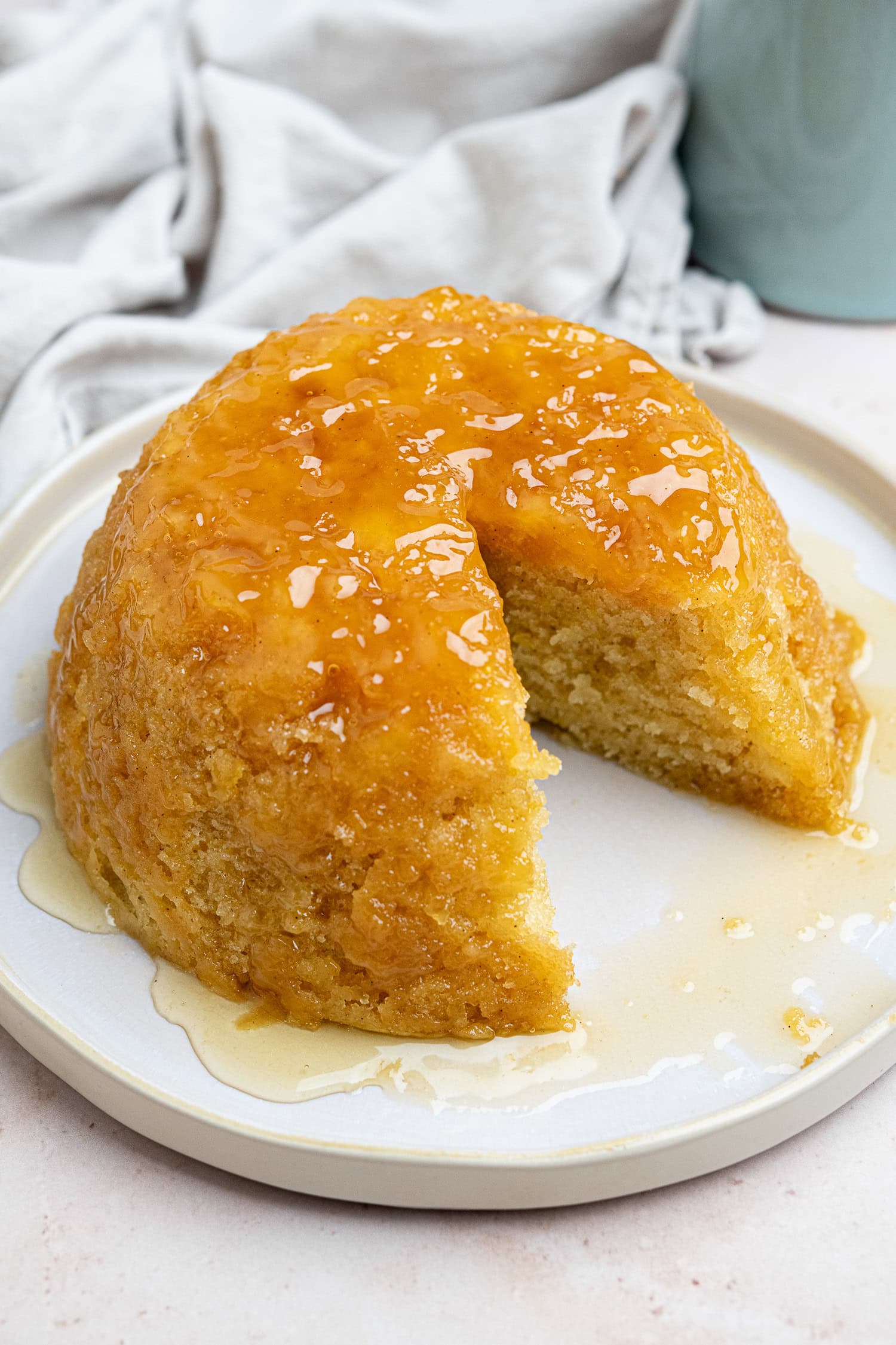 Steamed syrup sponge pudding on a white plate with a slice removed.