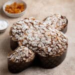 Vegan Colomba Pasquale on a brown surface with bowls of candied peel and pearl sugar.