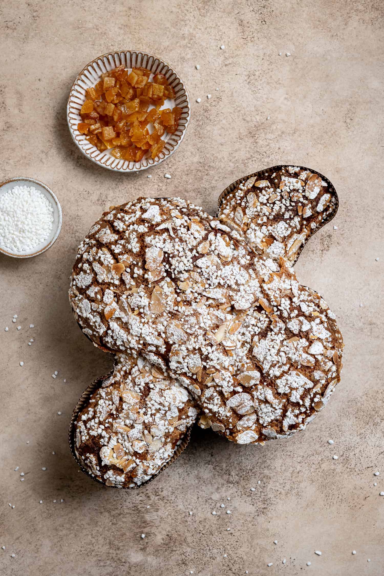 Flatlay of a vegan Colomba Pasquale with bowls of candied peel and pearl sugar.