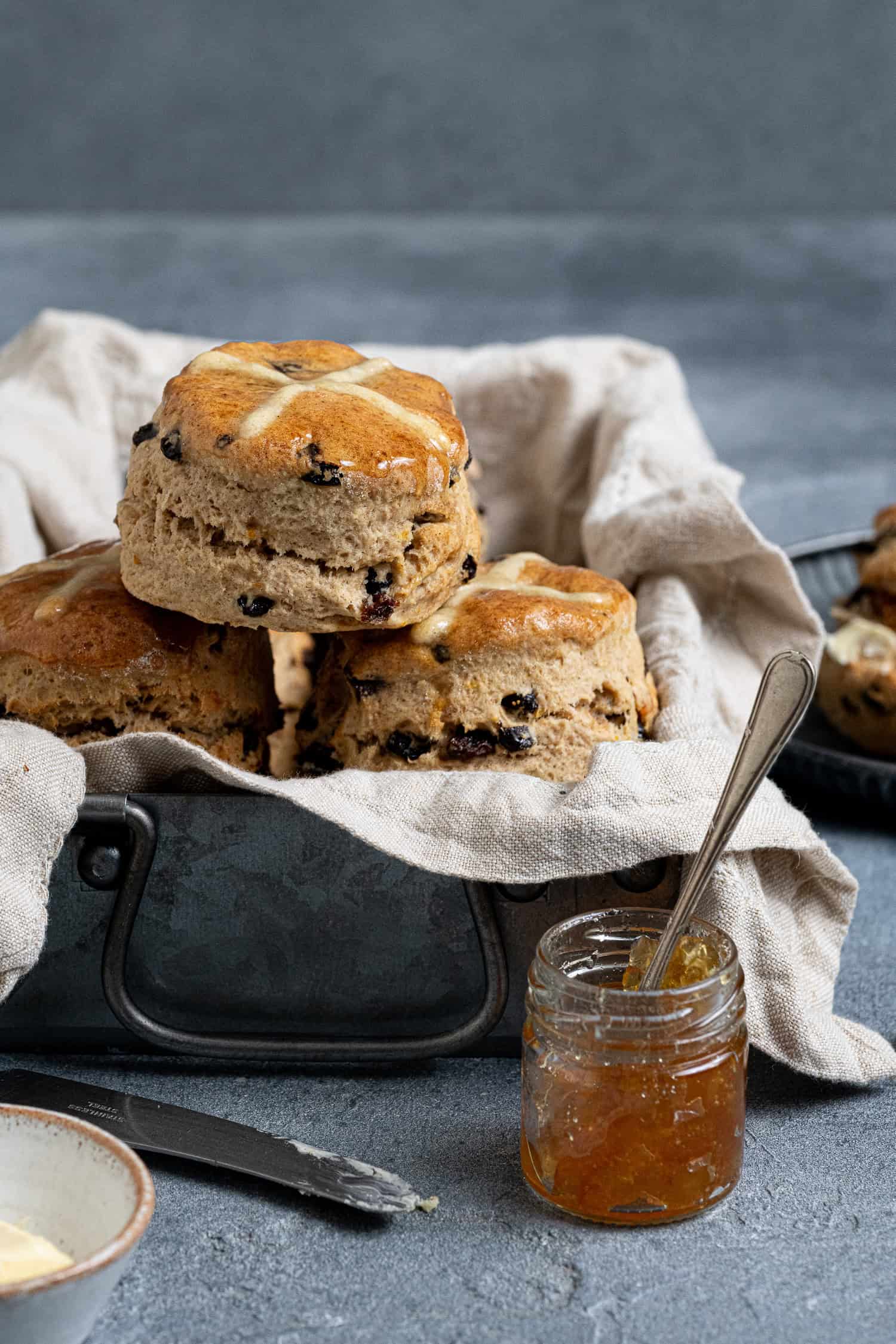 Hot cross scones in a metal box with a jar of marmalade and a bowl of butter.