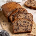Sliced vegan chocolate chip banana bread on a sheet of baking paper with a bowl of chocolate chips.