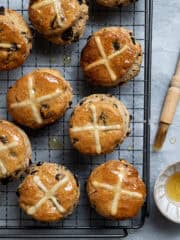 Vegan hot cross scones on a wire cooling rack with a bowl of syrup and a pastry brush.