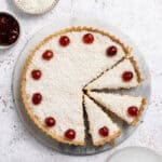 The sliced vegan Manchester tart on a marble board with bowls of coconut and glace cherries.