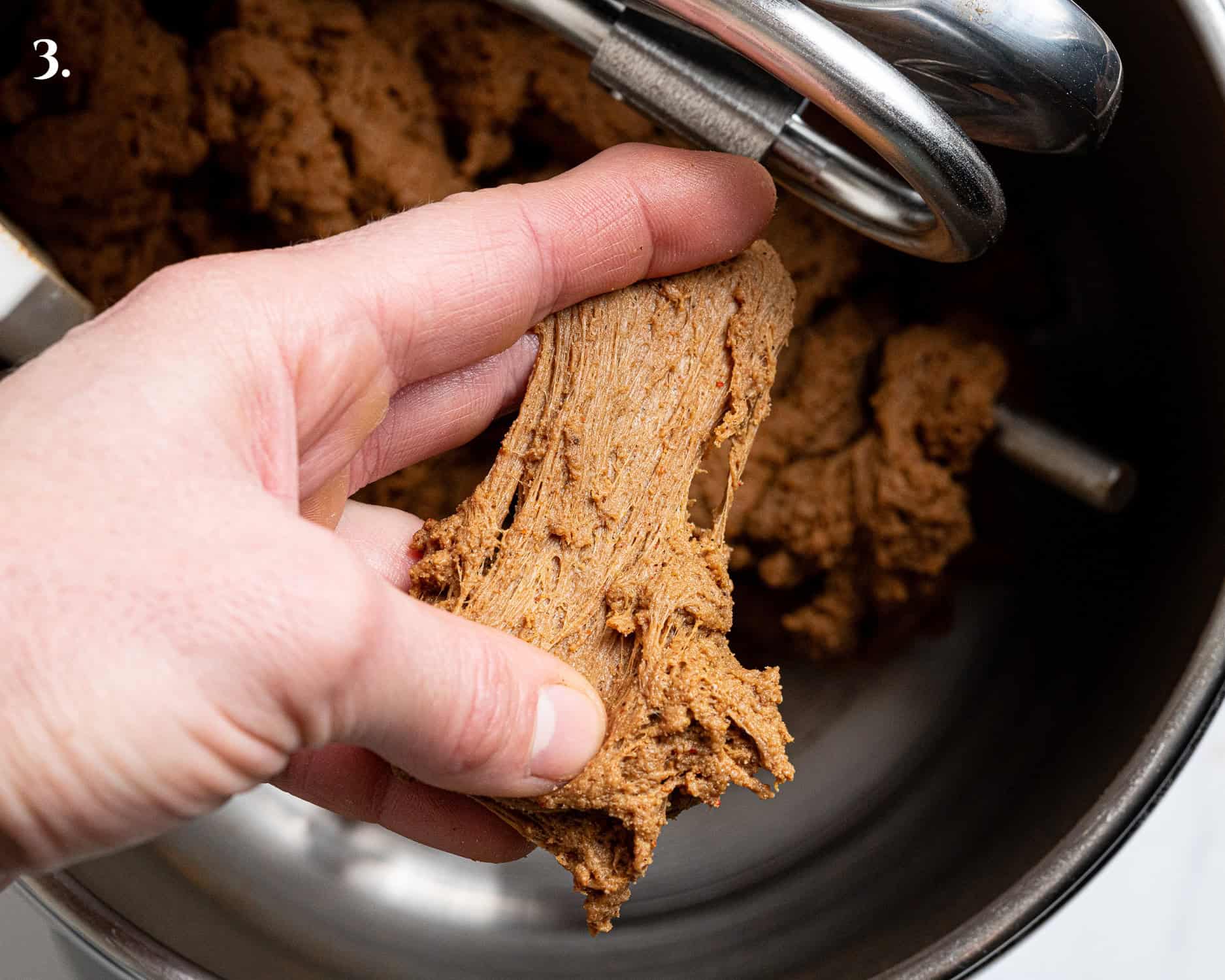 Step 3, a hand stretching a portion of the dough to show the stringy texture.