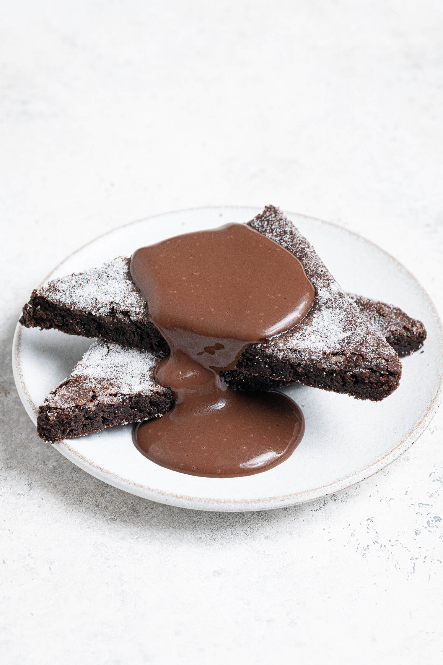 Two slices of vegan chocolate concrete on a white pplate with chocolate custard on top.
