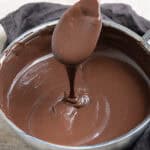 A pan of vegan chocolate custard with a spoon being lifted out of the pan.
