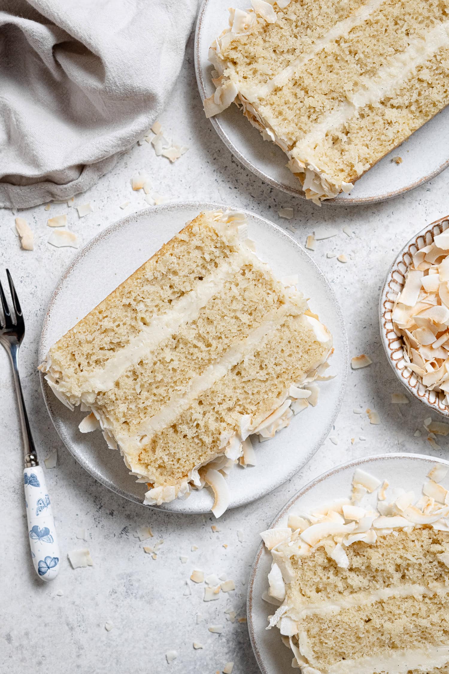 Three slices of vegan coconut cream cake on white plates.