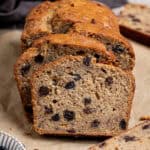 Sliced vegan rum raisin banana bread on a sheet of baking paper with a bowl of raisins.