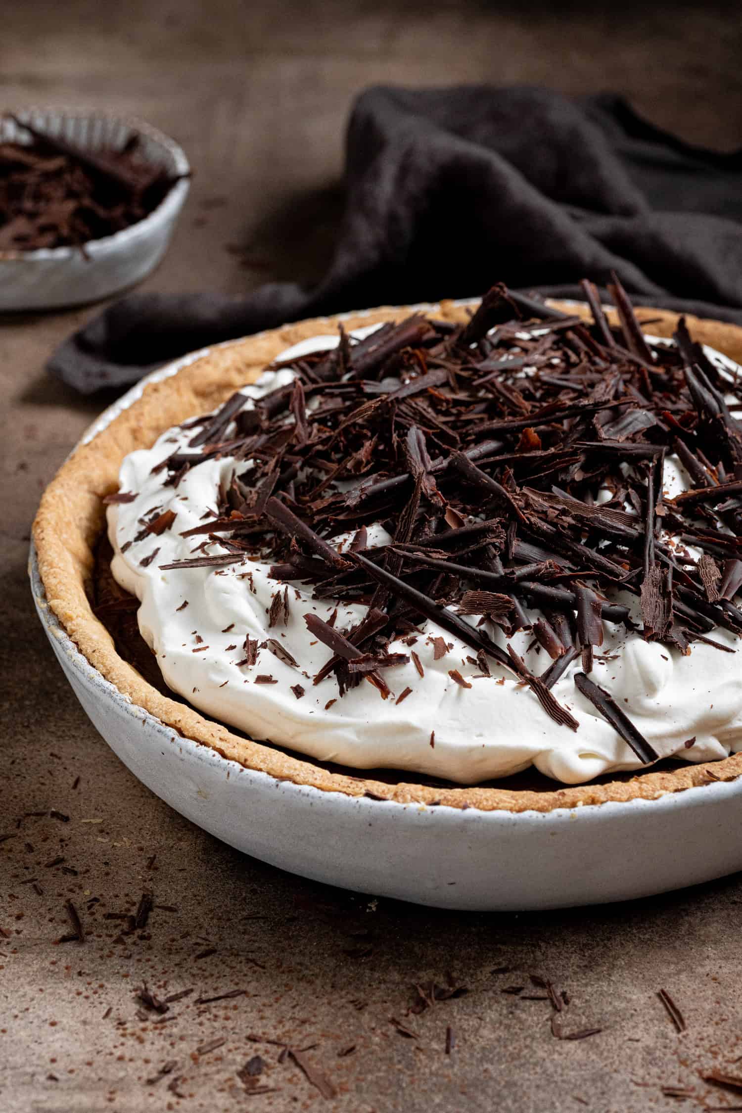 Vegan chocolate cream pie in a ceramic pie dish with a bowl of chocolate shavings.