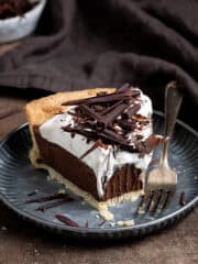 A slice of vegan chocolate cream pie on a metal plate with a forkful removed.